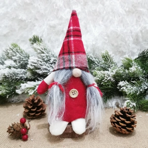 Close-up of Nordic faceless Christmas gnome with red plaid hat among pine cones and berries