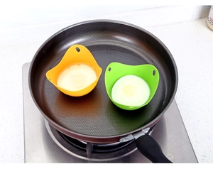 Cooking eggs in yellow and green silicone egg poachers inside a frying pan