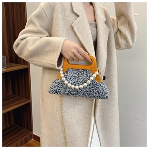 Close-up of black and white tweed handbag with wooden handle and elegant pearl chain trim