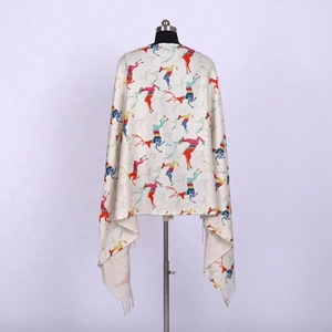 Detail of beige cashmere-like scarf featuring colorful reindeer patterns and tassel fringe