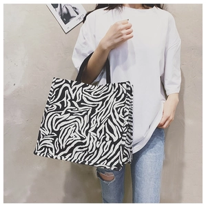 Detail of zebra print tote bag with black canvas straps against a grey textured wall