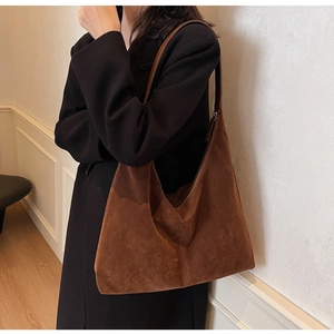 Detail view of large brown suede hobo bag worn with black coat for stylish commute