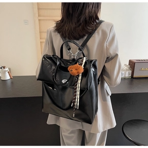 Detailed back view of a black glossy leather backpack with a plush bear pendant