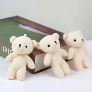 Detalle de tres mini ositos de peluche crema con lazos colgantes sobre un libro decorativo