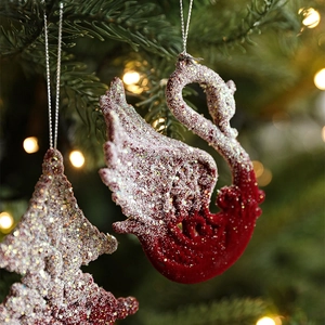 Red flocked swan and tree Christmas ornaments with artificial snow on a festive tree