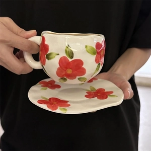 Detail of hand-painted floral ceramic cup and saucer set with gold rim and red flowers