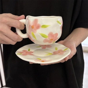 Close-up of hand-painted floral ceramic coffee cup with matching wave-edged saucer