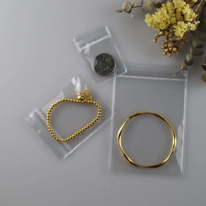 Three transparent PVC jewelry storage bags in different sizes on a decorative grey surface