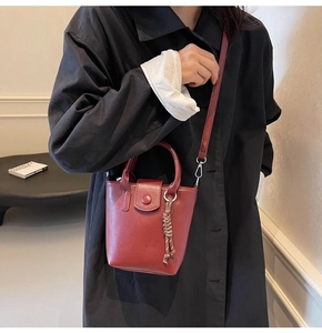 Detail of red leather bucket bag with top handle and woven rope charm held by model