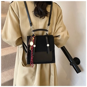 Detalle de mochila negra de retazos con solapa mate y un colgante tejido colorido