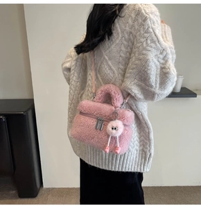 Detailed close-up of a pink plush crossbody bag featuring a cute furry charm and silver zipper
