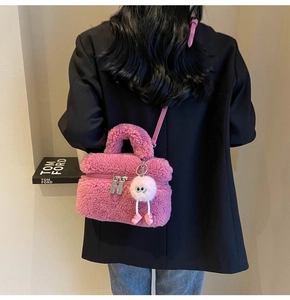 Pink faux fur crossbody bag with pom-pom charm shown on a model wearing a black blazer