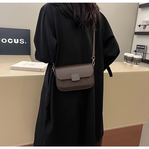 Detail of vintage dark brown crossbody bag with gold hardware worn on a black coat