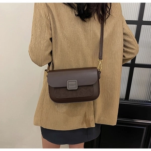 Brown faux leather crossbody bag with suede patchwork and gold buckle shown on a model