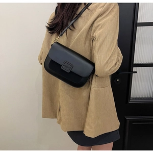 Detail view of a black leather crossbody bag on a model wearing a camel blazer