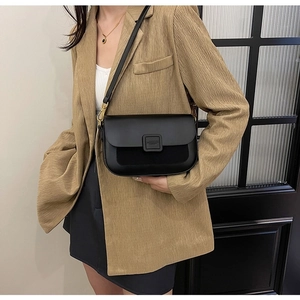 Detailed shot of black crossbody bag worn with brown blazer showing leather texture