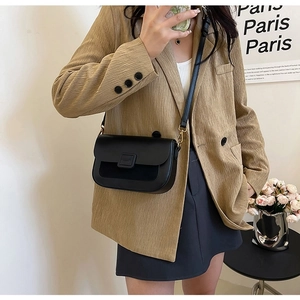 Model wearing a black crossbody flap bag with gold hardware and mixed leather textures