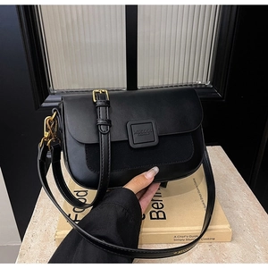Close-up of black leather crossbody bag with bronze gold buckle on stone surface