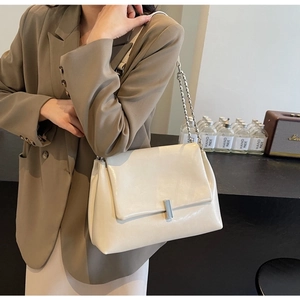 Detail of a beige PU leather chain bag with a silver square lock on a stylish model