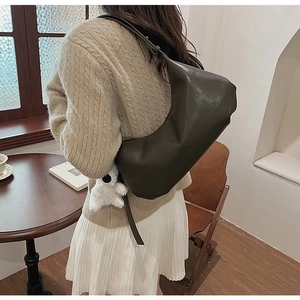 Detail of dark olive green shoulder bag with plush pendant on soft material