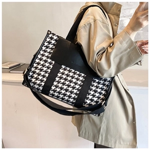 Detail shot of a black and white houndstooth crossbody bag with black leather flap on a model