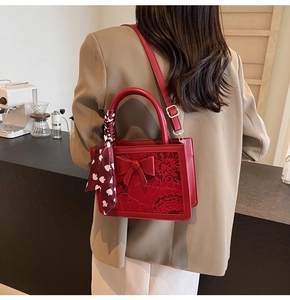 Close-up of red embroidered bridal handbag featuring 3D bow and silk scarf wrapped handle