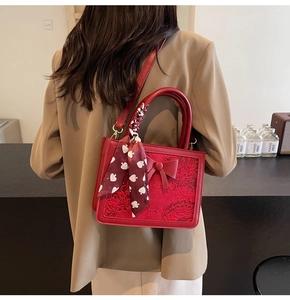 Detail of red bridal handbag with floral embroidery and silk scarf accent on model