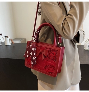 Detail of red bridal handbag with floral embroidery and silk scarf handle on a shoulder strap