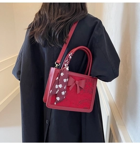 Detail of red bridal handbag featuring a textured bow and heart-print silk scarf handle