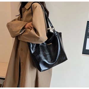 Minimalist black tote bag in soft leather shown on shoulder with long coat style