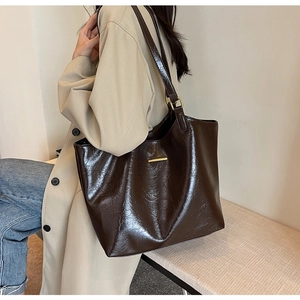 Detail of soft brown leather tote bag with metallic bar on beige trench coat outfit