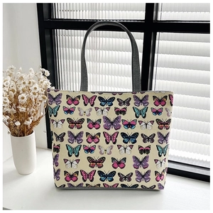 Detail of canvas tote bag with vibrant butterfly print and sturdy grey handles on windowsill