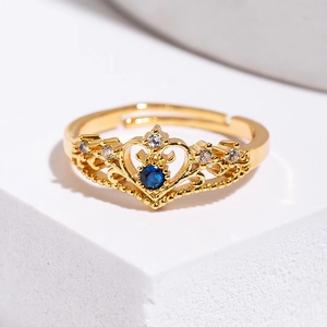 Golden crown ring with a blue gemstone and small diamonds on a white geometric background