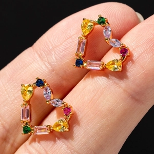Golden heart stud earrings with colorful zircon gemstones held on a fingertip