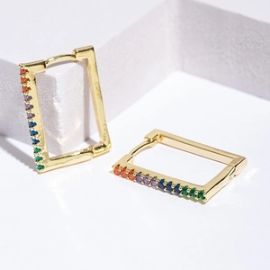 Rectangular gold huggie earrings with rainbow zircon stones on white geometric props