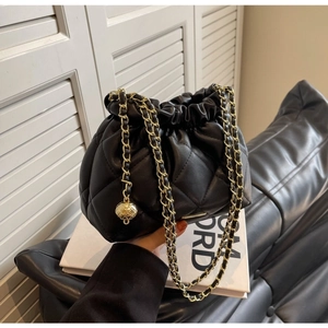 Detail of black quilted leather bucket bag with gold chain strap and spherical charm ornament