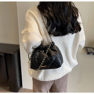 Close-up of black quilted bucket bag with gold chain strap on a model shoulder