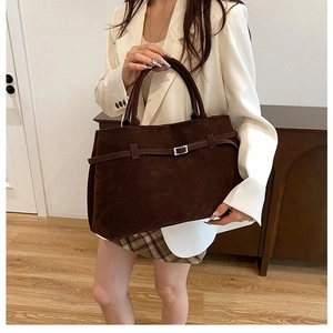 Detail of a large dark brown suede tote bag featuring a decorative strap and silver buckle