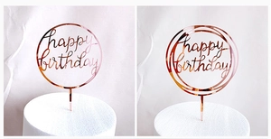Close-up of two rose gold acrylic Happy Birthday cake toppers with sleek circular designs