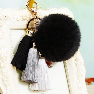 Detail of a large black plush pompom with silk tassels on a golden metal keychain