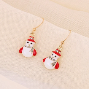 Macro detail of snowman earrings with red hat and scarf on beige textured fabric