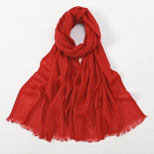 Detail view of a soft red slub cotton scarf featuring woven texture and fringe trim