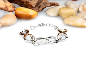 Close-up of polished silver infinity bracelet on white surface with natural pebbles