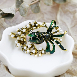 Detailed shot of an ornate goldfish brooch with green enamel and white pearls