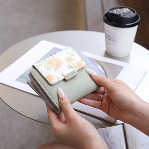 Short PU leather floral wallet with gold clasp shown in a lifestyle coffee shop setting