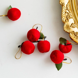 Red flocked Christmas apple ornaments with gold string and green leaves on white background