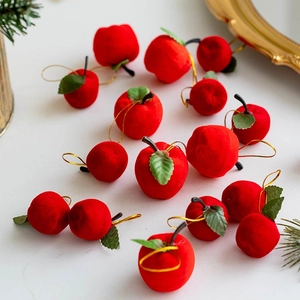 Red flocked Christmas apple ornaments with gold cords and green leaves on white background