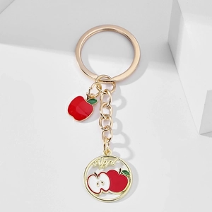 Detailed close-up of a golden apple keychain with red enamel fruits on white background