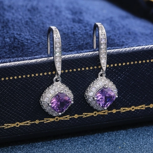 Macro shot of square purple zircon earrings with pavé crystals on a blue gift box