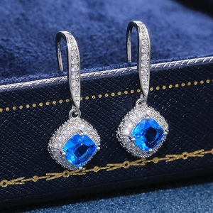 Macro detail of square blue zircon earrings with halo diamond setting on a velvet jewelry box